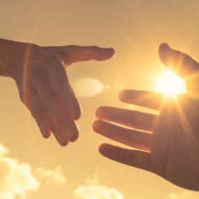 two hands reaching for each other with sunlight in the background